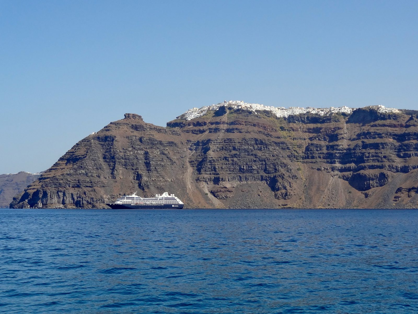 A cruise ship in the deep-blue caldera beneath the cliffs of Santorini